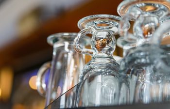 Close-up of several clear glass mugs upside down on a shelf, with soft lighting and blurred background.